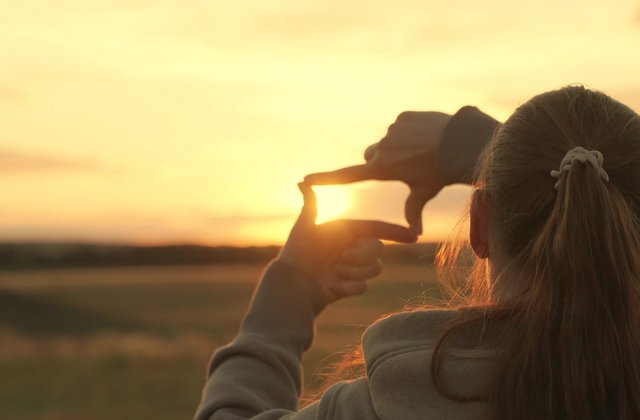 Junger Mensch zeigt mit seinen Fingern das Symbol für einen Rahmen, der den Sonnenuntergang im Park festhält