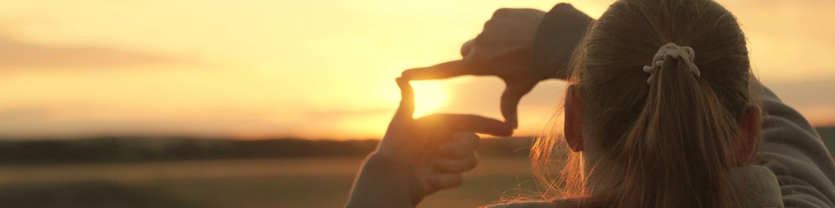 Junger Mensch zeigt mit seinen Fingern das Symbol für einen Rahmen, der den Sonnenuntergang im Park festhält