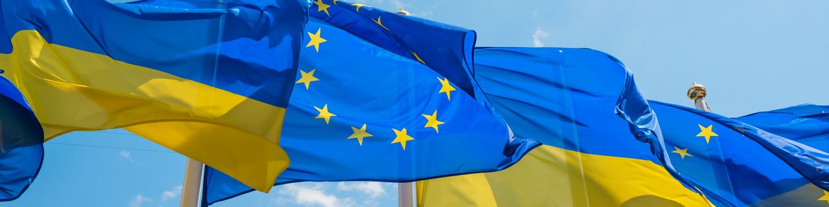 Reihe von Fahnenmasten mit Flaggen der Europäischen Union und der Ukraine, die vor dem Hintergrund eines blauen Himmels im Wind wehen