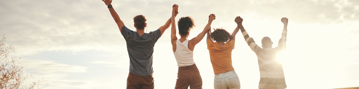 Mehrere junge Menschen, die sich für Teamarbeit und Nachhaltigkeit an den Händen halten, bei Sonnenuntergang