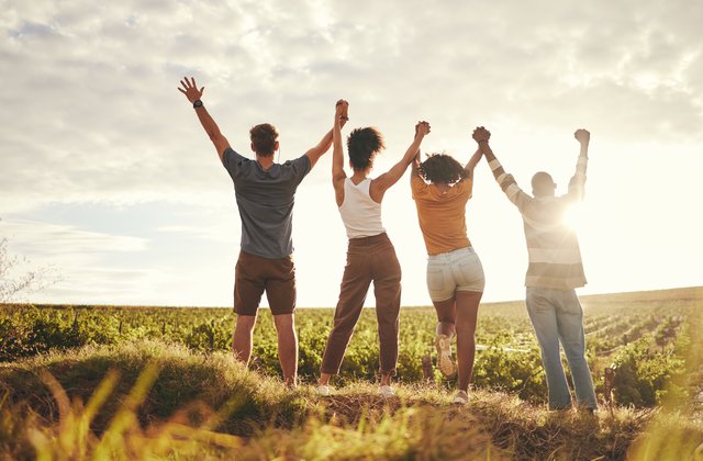 Mehrere junge Menschen, die sich für Teamarbeit und Nachhaltigkeit an den Händen halten, bei Sonnenuntergang