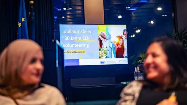 Zwei Teilnehmerinnen sitzen vor der Leinwand Jubiläumsfeier "30 Jahre EU-Volunteering"
