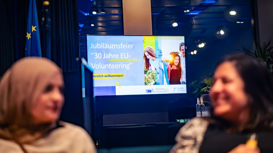Zwei Teilnehmerinnen sitzen vor der Leinwand Jubiläumsfeier "30 Jahre EU-Volunteering"