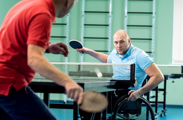 Erwachsene Person mit Behinderung im Rollstuhl spielt mit ihrer Trainingsperson Tischtennis