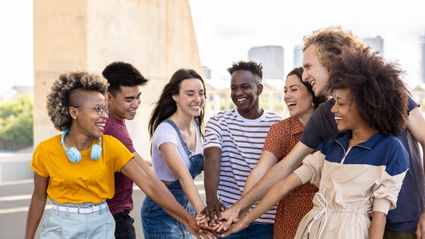 Gruppe junger Menschen mit aufeinandergelegten Händen als Zeichen für Einheit steht gemeinsam auf einer Straße in der Stadt