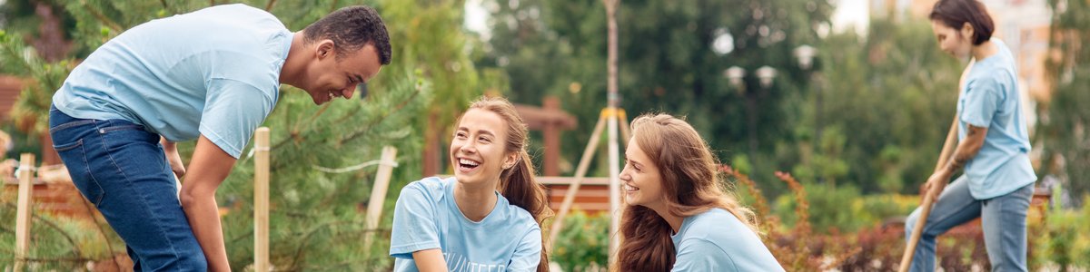 Junge Freiwillige pflanzen draußen Bäume, graben Erde um und unterhalten sich fröhlich