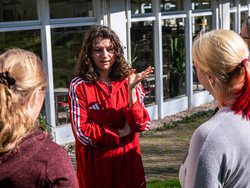 Vier Personen stehen auf einer Wiese. Eine Person spricht und drei weitere hören ihr zu.