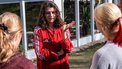 Vier Personen stehen auf einer Wiese. Eine Person spricht und drei weitere hören ihr zu.