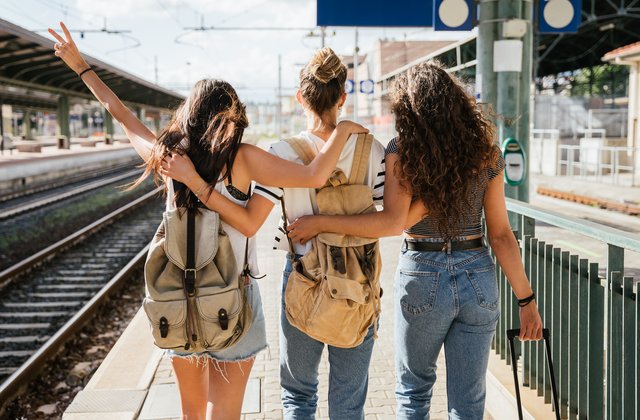 Drei junge Menschen am Bahnhof, die den Zug für ihre gemeinsame Reise nehmen