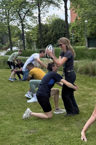Junge Menschen in Sportkleidung machen Übungen auf einer Rasenfläche mit einem Rugby