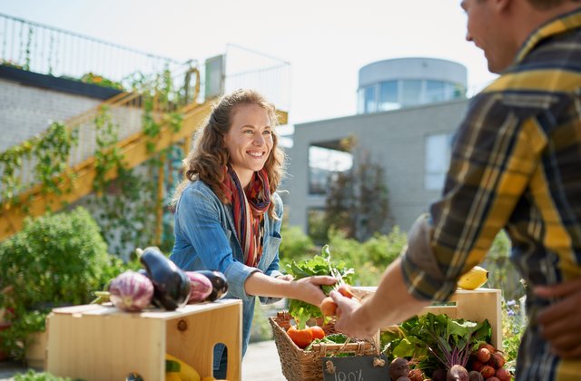 Freundlicher junger Mensch, der einen Bio-Gemüsestand auf einem Markt betreut