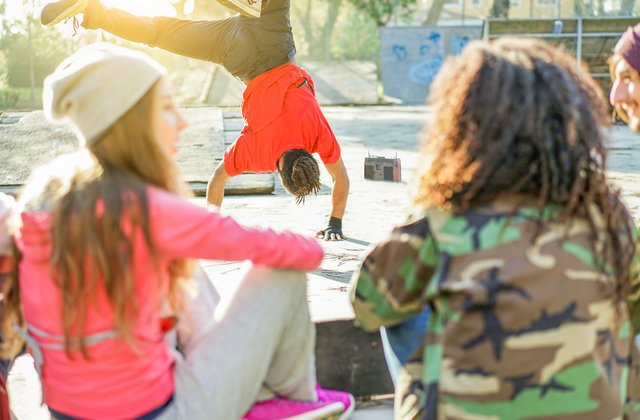 Glückliche junge Menschen hören Musik mit breakdancender Person im Hintergrund