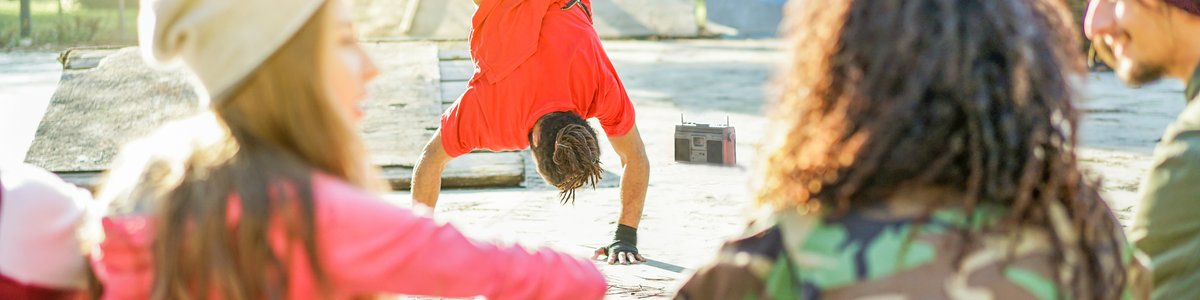 Glückliche junge Menschen hören Musik mit breakdancender Person im Hintergrund