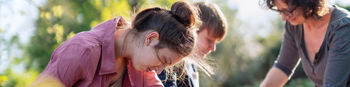 Eine junge Person hilft anderen beim Bau von Holzbehältern für ihren Permakultur-Gemüsegarten.
