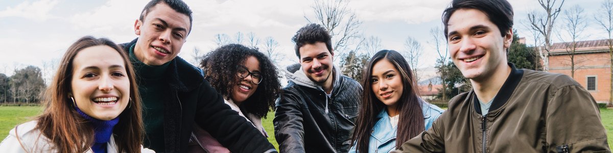 Eine Gruppe junger Menschen im Park fasst sich in der Mitte eines Kreises an den Händen und hat gemeinsam Spaß