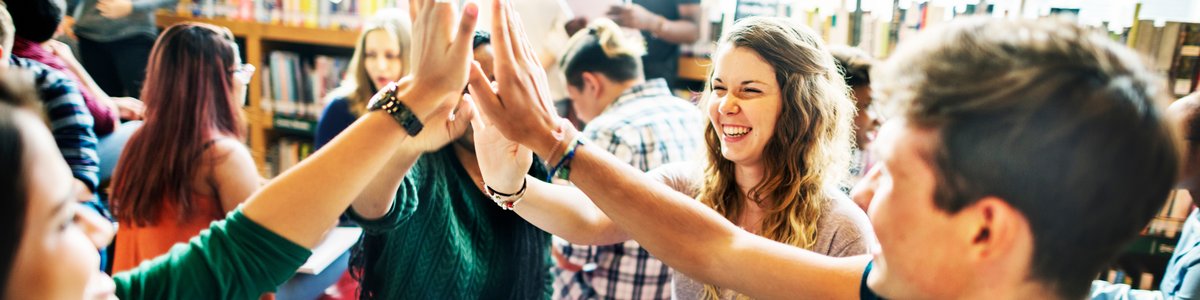 Mehrere junge Menschen sitzen zusammen und geben sich fünf