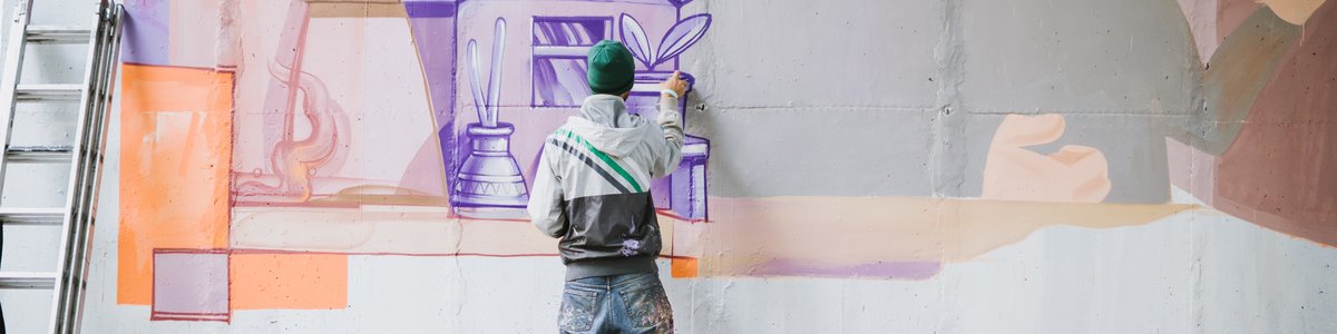 Ein junger Mensch sprüht bunte Motive auf eine Wand