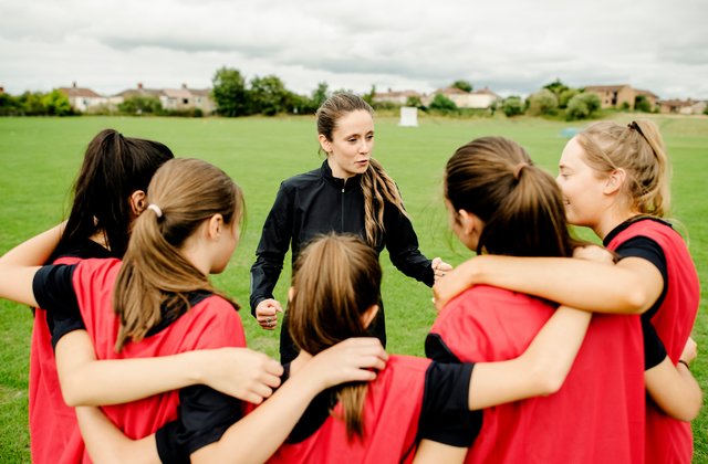 Rugbyspielende und ihre Trainingsperson versammeln sich vor einem Spiel