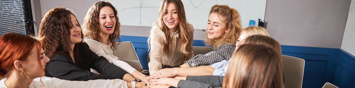 Fröhliches Team kreativer junger Menschen, das sich über einen Tisch mit Laptops hinweg die Hände reicht